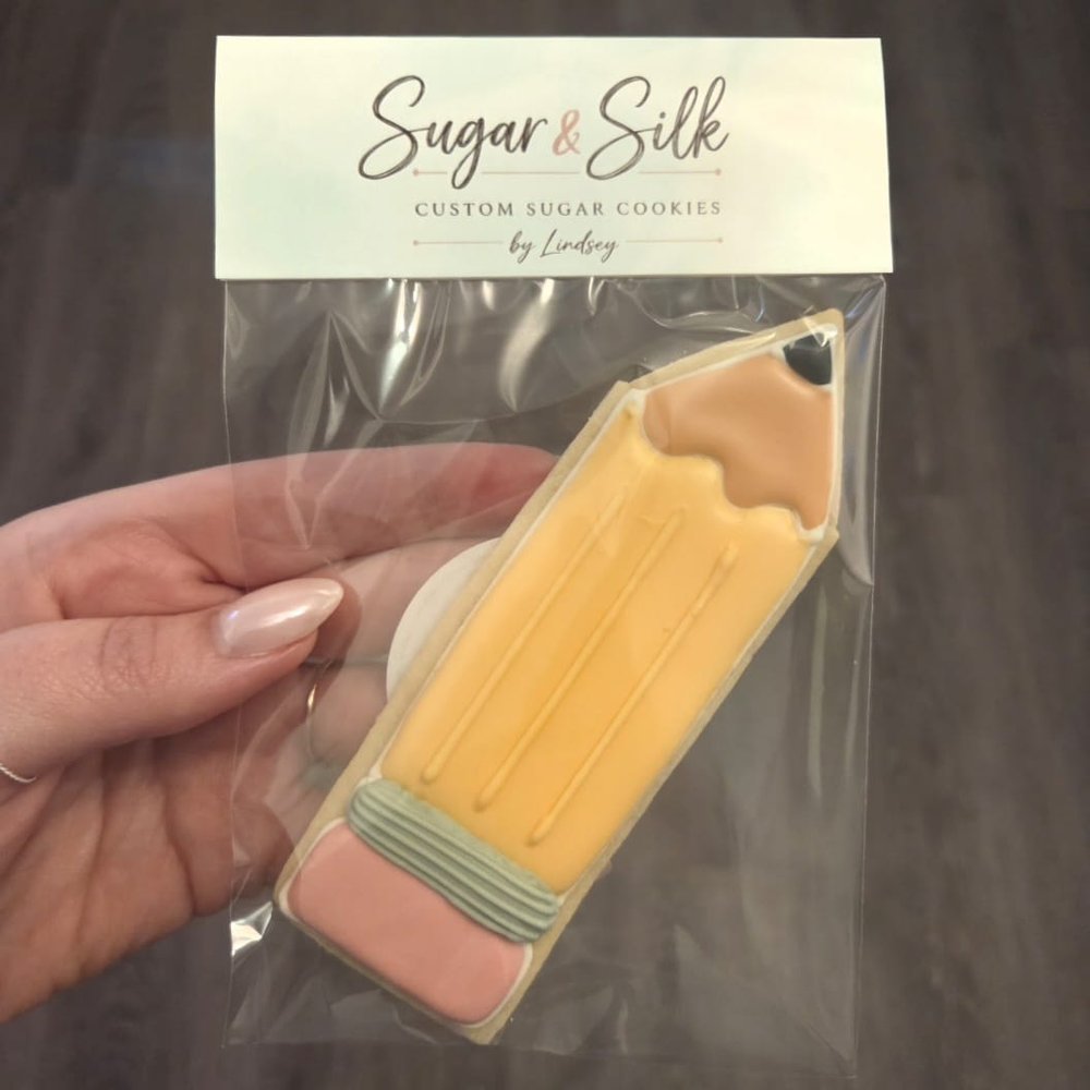A pencil cookie in a clear bag with the Sugar & Silk custom sugar cookies label